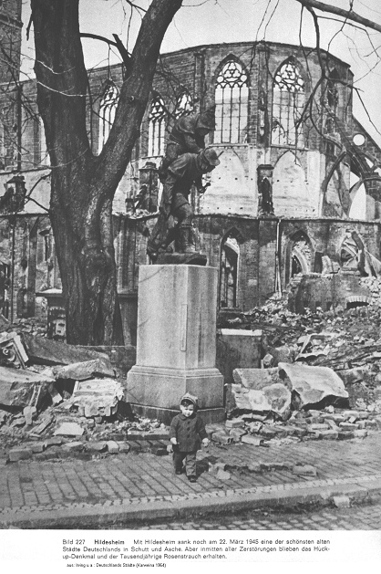 Das Huckup-Denkmal von Hildesheim steht
                        nach dem Feuersturm vom 22. Mrz 1945 intakt
                        mitten in Ruinen, im Hintergrund die Ruine der
                        Andreaskirche