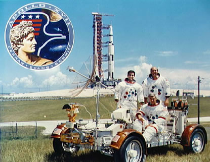 Entrenamiento de Apolo 17: "Carro
                        lunar" en un prado, al fondo hay una
                        plataforma de lanzamiento, foto en color con los
                        "astronautas" Eugene A. Cernan, Ronald
                        E. Evans, y Harrison H. Schmitt.