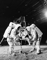Trainingsfoto aus der Mondhalle in Houston
              (Geb�ude 9) mit Armstrong und Aldrin beim
              "Training" f�r Apollo 11 auf dem Mondboden.
              Rechts oben strahlt ein grosser Scheinwerfer als
              "Sonne" mit fotografischem Strahleneffekt.