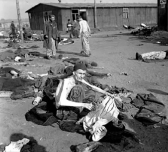 Emaciated German captive
                sitting on the ground in a Rhine meadow camp in summer
                1945